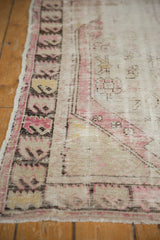 Vintage distressed Oushak rug corner with worn plum, ivory, charcoal geometric motifs, and intact selvage.