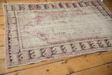 Distressed vintage Oushak rug featuring faded plum, ivory, and charcoal patterns with wear.