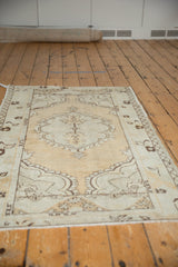 Distressed vintage Oushak rug corner with scalloped medallion, dusty gold, ivory, and even wear.