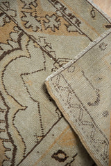 Corner of Distressed Oushak rug reveals worn dusty gold pile and hand-knotted foundation.