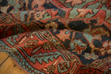 Antique Heriz rug's hand-knotted pile showing wine red, mallard green, and time-softened texture.