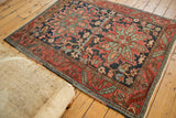 Antique Heriz rug corner displays serrated leaf border in red, dusty navy, and green.