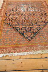 Close-up of vintage Malayer rug's beige fringe showing staining and patterned border.