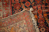 Flipped corner of a vintage Malayer rug, revealing navy Herati pile, woven foundation, and fringed end.