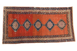 Antique Bakshaish rug with diamond medallions on a worn, abrashed madder red field and navy wave borders.