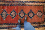 Scale view of a worn antique Bakshaish rug with repeating navy diamond medallions on an abrashed red field.