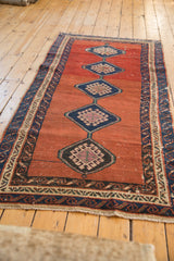Long angle view of an antique Bakshaish rug with repeating diamond guls and a running wave border.