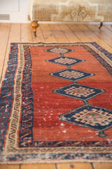 Running wave border alongside repeating diamond medallions on an antique Bakshaish rug's abrashed red field.