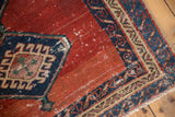 Corner of an antique Bakshaish rug with a running wave border and a worn, madder red field.