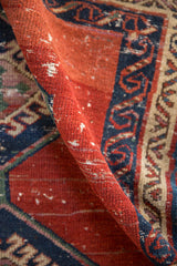 Textured wear to knot heads on the red pile alongside the navy running wave border of the rug.