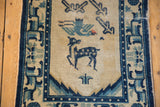 Pictorial deer and bird motif in cobalt blue and ivory on vintage rug, with visible wear.