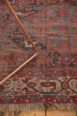 Worn antique Qashqai rug with ruby red field, faded animal motifs, and fringed edge.