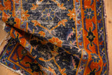 Folded vintage rug detail: cobalt blue field, tangerine palmette border, visible foundation wear.