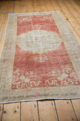 Vintage distressed Oushak rug viewed lengthwise, showing its raspberry red field and ivory medallion.