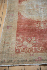 Corner detail of a distressed Oushak rug with faded raspberry red motifs and worn pile.