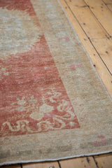 Distressed Oushak rug corner with raspberry red cloud-band motifs and visible knot heads.