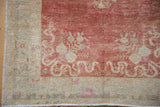 Corner of a distressed Oushak rug showing the worn low pile, ivory border, and raspberry red cloud-band designs.