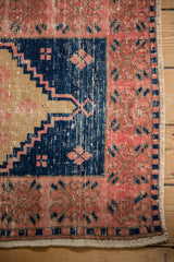 Distressed vintage Oushak rug corner, blush border, navy geometric motifs, intact selvage.