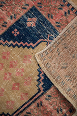 Distressed blush and navy geometric patterns of a vintage Oushak rug, revealing its hand-knotted back.