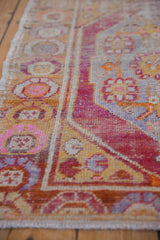 Distressed vintage Oushak rug's pile, revealing knot heads, fuchsia, gold, and pale blue patterns.