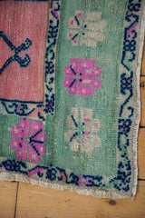 Distressed Oushak rug corner showing worn rose, mint green, pink floral patterns and selvage.