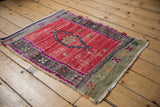 Distressed cherry red Oushak rug corner, revealing textured pile, green border, and geometric accents.
