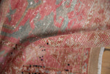 Distressed Oushak rug's rolled edge, showing worn pile with blush, silver, and raspberry.