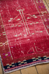 Distressed cherry red Oushak rug detail highlighting wear and navy, beige checkerboard border.