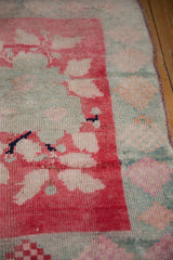 Distressed Oushak rug close-up: blush-red floral border, muted blue-green field, low pile.