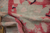 Distressed Oushak rug's folded hand-knotted texture, revealing blush, cherry red, and muted blue pile.