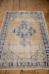 Distressed Oushak rug with navy blue scalloped medallion and wear on dusty gold field.