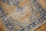 Vintage distressed Oushak rug corner, showing exposed foundation, faded gold, and navy blue.