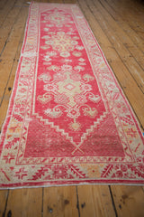 End detail of distressed Oushak runner with worn cherry red field and ivory geometric border.
