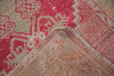 Distressed Oushak rug corner: worn cherry red pile, light visible foundation, and intact selvage.