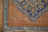 Distressed tangerine Oushak rug corner with visible wear, blue border, and ivory fringe.