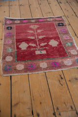 Distressed Oushak rug's worn texture, cranberry red field, and colorful plant and floral motifs.