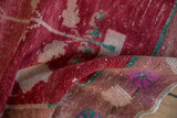 Folded vintage Oushak rug showing distressed fuchsia, cranberry red, and beige pile.