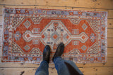 Feet on vintage distressed Oushak rug, featuring madder red, ivory, and pale blue geometric designs.