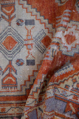 Folded vintage distressed Oushak rug showcasing geometric madder root red and ivory patterns.