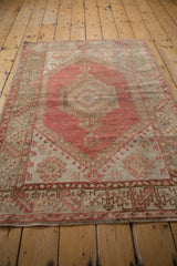 Distressed Oushak rug's bottom border, featuring serrated leaves, dusty raspberry, beige, and secured fringe.