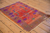 Distressed Oushak rug detail: playful green vine, magenta floral, and vibrant geometric border motifs.