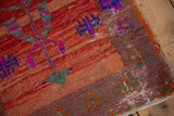 Distressed pile showing geometric green and tangerine motifs at a vintage Oushak rug's corner.