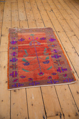 Distressed Oushak rug corner with geometric floral motifs in fuchsia, blue, and orange.