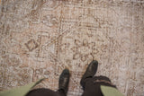 Close-up of vintage distressed Oushak rug, showing worn texture and faded beige floral motifs.