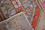 Distressed Oushak rug pile with rust and lavender, showing hand-knotted back and selvage.