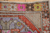 Distressed Oushak corner with rust, fuchsia, and lavender geometric patterns and worn pile.