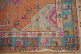 Distressed Oushak rug corner, tangerine field with serrated leaves, and geometric seafoam borders.