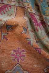 Textured pile of a distressed Oushak rug showing tangerine orange, seafoam green, and magenta motifs.