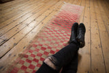 Distressed Oushak runner with a worn checkered pattern in cherry red and beige.