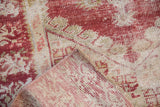 Distressed Oushak pile in cherry red and ivory, revealing woven foundation and secured edge.